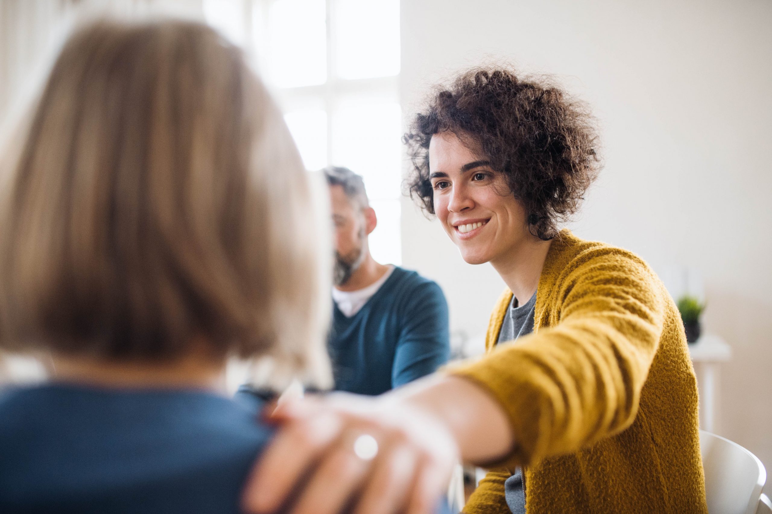 Smiling woman with reassuring hand on client's shoulder during group therapy