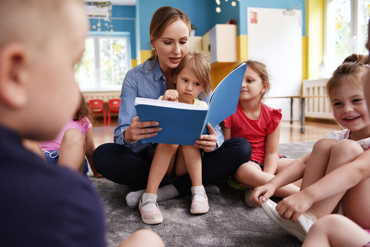 Kids and teacher reading a book together in preschool
